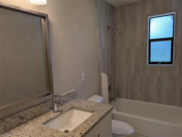Full bath featuring vanity, toilet, a textured wall, and bathtub / shower combination