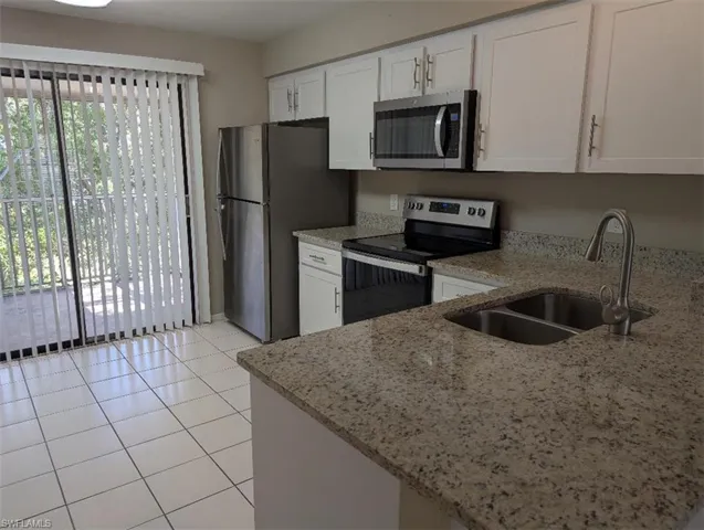 Kitchen featuring white cabinetry, light stone counters, stainless steel appliances, and a sink