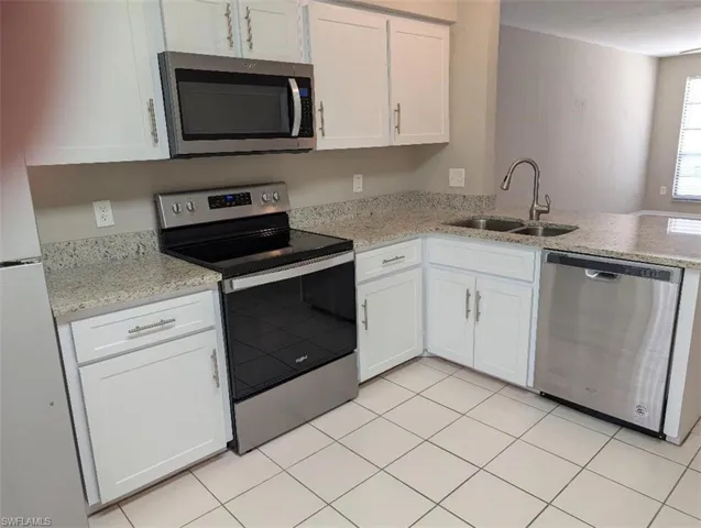 Kitchen featuring light stone counters, a sink, a peninsula, stainless steel appliances, and white cabinets