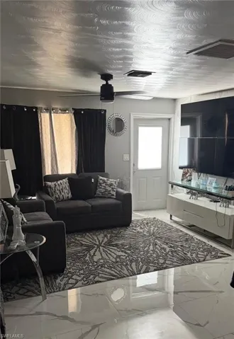 Living area featuring polished marble-look flooring, a ceiling fan with integrated lighting, a contrasting dark accent wall, and a white paneled door