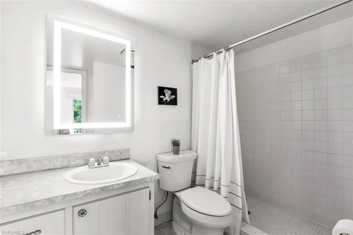 Bathroom featuring curtained shower, toilet, and vanity
