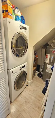 Laundry room featuring water heater, stacked washer and dryer, and light wood-type flooring