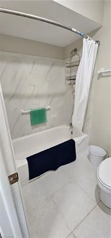 Bathroom with tile patterned floors, shower / tub combo with curtain, and toilet