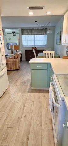 Kitchen featuring green cabinets, light hardwood / wood-style flooring, fridge, decorative light fixtures, and range