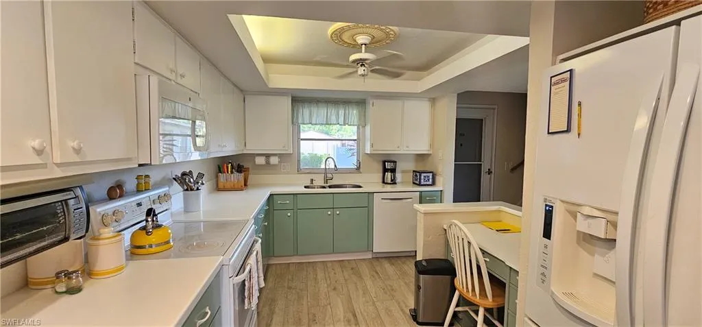 Kitchen with white cabinetry, a raised ceiling, green cabinets, light hardwood / wood-style flooring, and white appliances