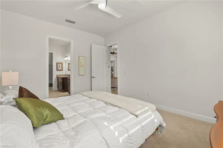 Bedroom featuring light carpet, visible vents, ensuite bath, and baseboards