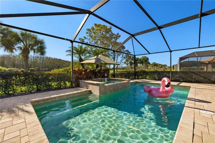 View of swimming pool featuring glass enclosure, a patio, and a pool with connected hot tub