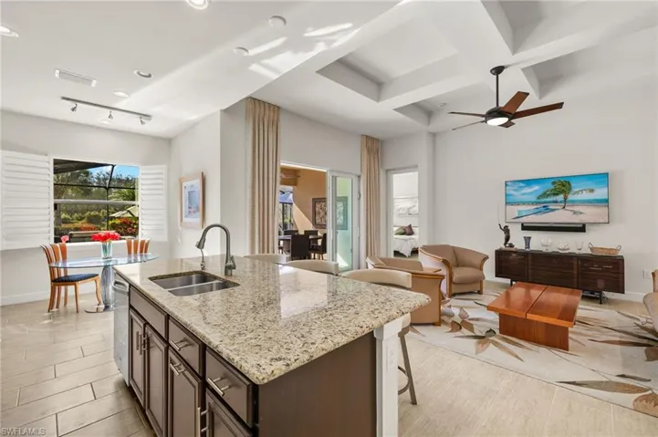 Kitchen with light stone counters, visible vents, coffered ceiling, a sink, and open floor plan