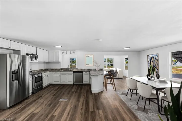 Kitchen featuring stainless steel appliances, white cabinets, a peninsula, dark wood-type flooring, and dark stone counters