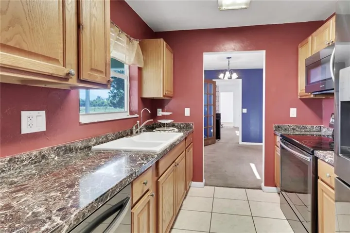 Kitchen featuring appliances with stainless steel finishes, light tile patterned floors, a chandelier, pendant lighting, and light colored carpet
