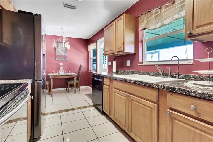 Kitchen with light tile patterned floors, appliances with stainless steel finishes, hanging light fixtures, a chandelier, and dark stone counters