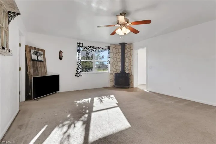 Unfurnished living room featuring a wood stove, carpet, and a ceiling fan
