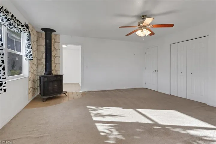 Unfurnished living room with a wood stove, carpet, tile patterned flooring, and a ceiling fan