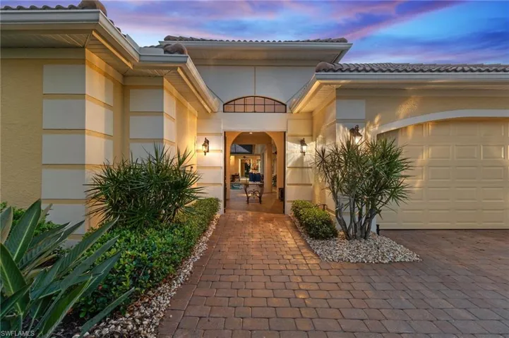 Exterior entry at dusk with a tiled roof, stucco siding, an attached garage, and decorative driveway