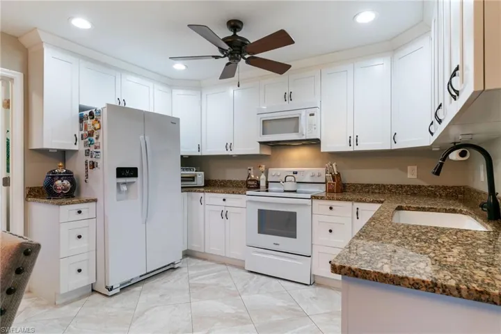 Kitchen featuring white appliances, a sink, a ceiling fan, white cabinets, and recessed lighting