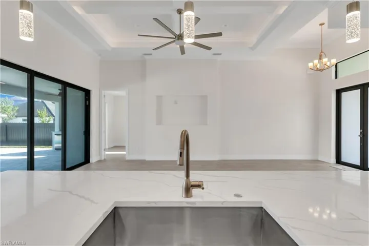 Kitchen featuring sink, light stone counters, crown molding, pendant lighting, and ceiling fan with notable chandelier
