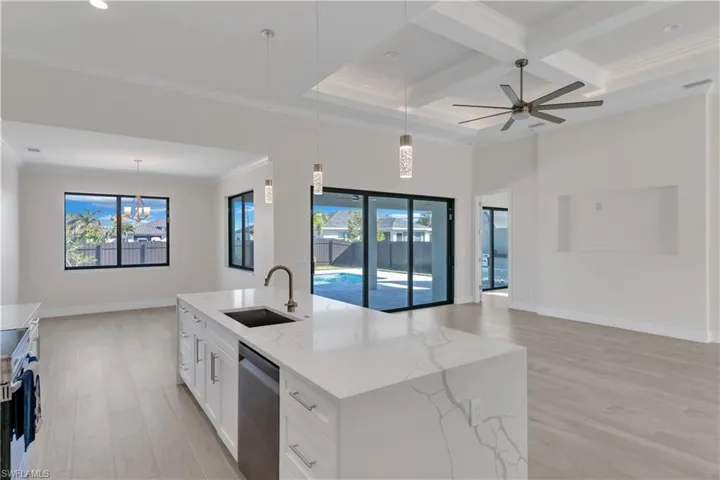 Kitchen featuring light stone counters, stainless steel dishwasher, a kitchen island with sink, sink, and hanging light fixtures