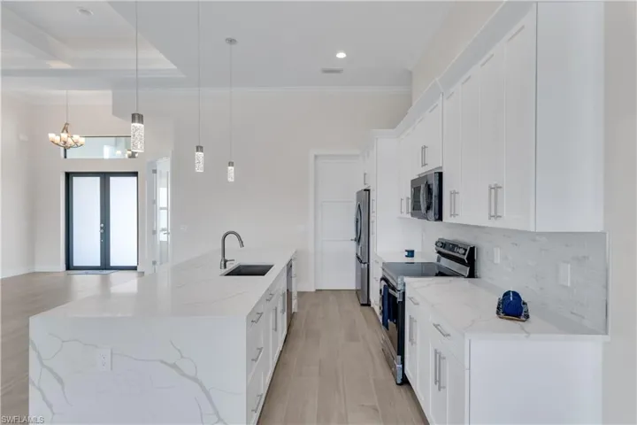 Kitchen featuring white cabinetry, sink, light stone countertops, hanging light fixtures, and stainless steel appliances