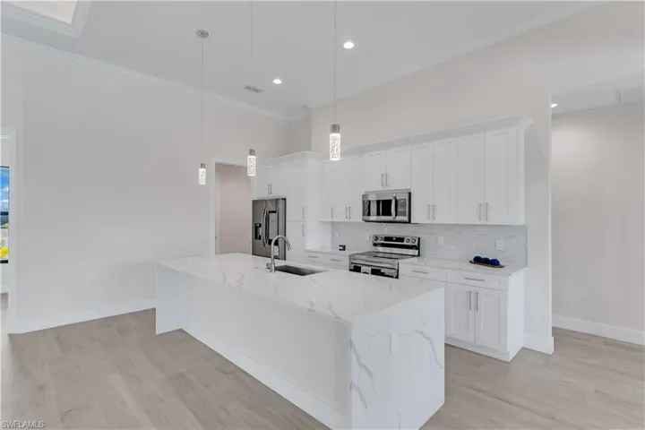 Kitchen featuring appliances with stainless steel finishes, a center island with sink, white cabinetry, and pendant lighting