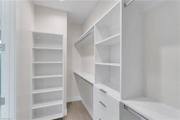 Walk in closet with light hardwood / wood-style flooring