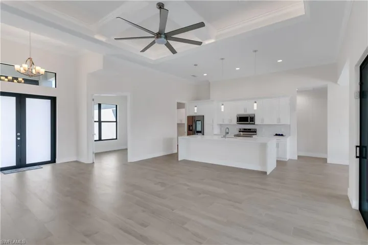 Kitchen featuring appliances with stainless steel finishes, coffered ceiling, pendant lighting, a center island with sink, and white cabinetry
