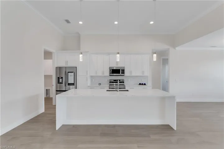 Kitchen featuring light stone countertops, appliances with stainless steel finishes, a spacious island, pendant lighting, and white cabinets