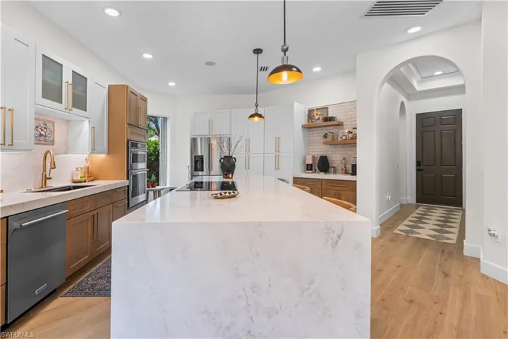 Kitchen with open shelves, light wood finished floors, appliances with stainless steel finishes, recessed lighting, and arched walkways