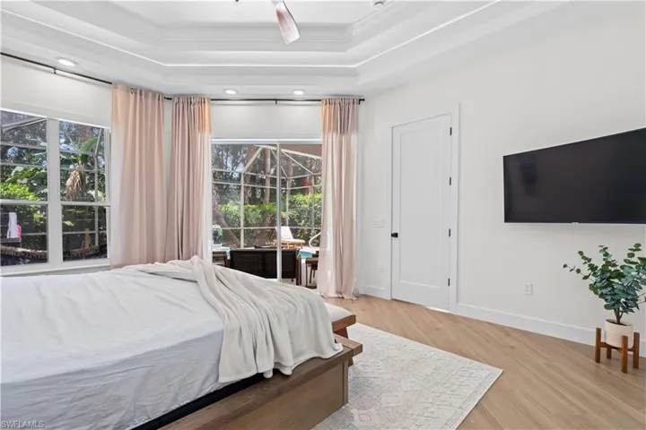 Bedroom with multiple windows, light wood-style floors, access to exterior, a raised ceiling, and ornamental molding