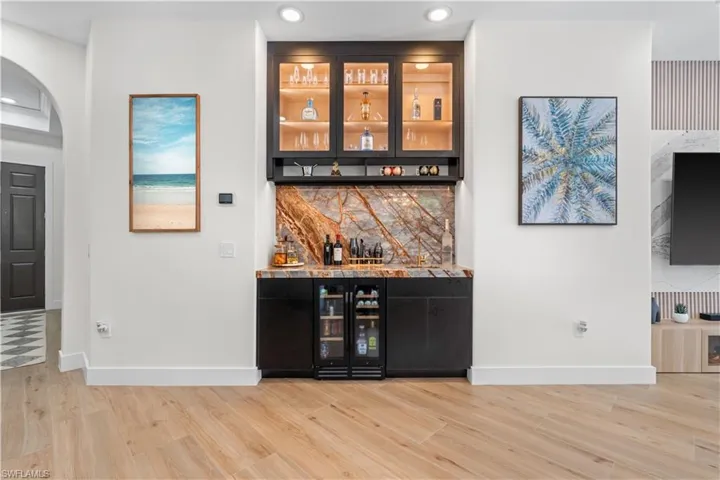 Indoor dry bar featuring decorative backsplash, beverage cooler, light wood-style flooring, arched walkways, and recessed lighting