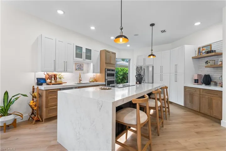 Kitchen with decorative backsplash, stainless steel appliances, light wood-type flooring, open shelves, and a breakfast bar area
