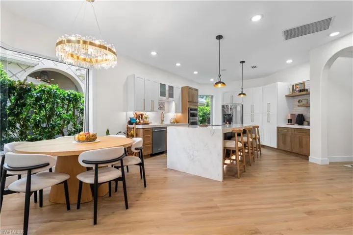 Kitchen with a breakfast bar area, a center island, open shelves, light wood-style floors, and glass insert cabinets