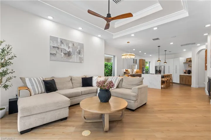 Living room featuring a raised ceiling, recessed lighting, ceiling fan, light wood finished floors, and arched walkways