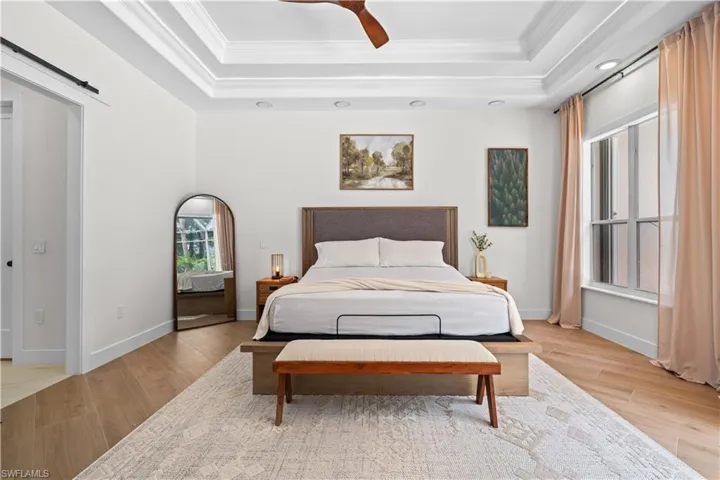 Bedroom with a barn door, a raised ceiling, ornamental molding, light wood-type flooring, and a ceiling fan