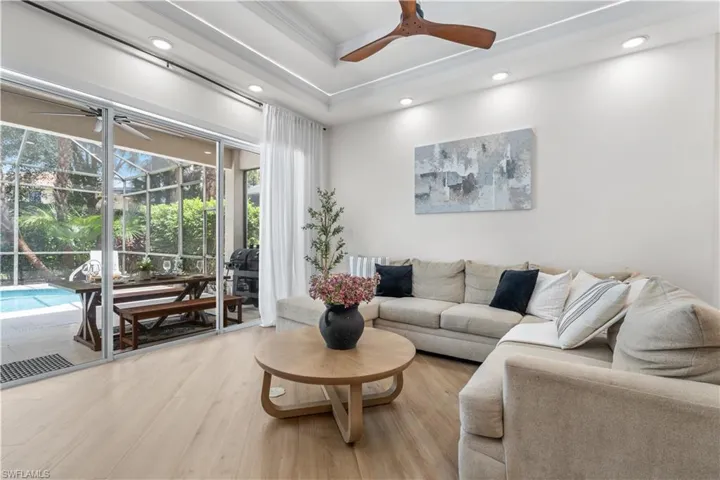Living area with ceiling fan, light wood-style floors, recessed lighting, a sunroom, and a tray ceiling