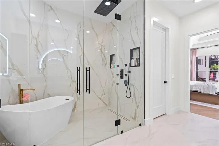 Ensuite bathroom featuring marble tiled floors, a marble finish shower, a soaking tub, recessed lighting, and stone wall