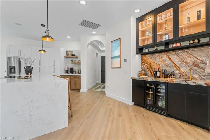 Indoor dry bar featuring tasteful backsplash, wine cooler, arched walkways, light wood-style flooring, and recessed lighting