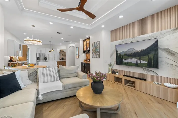 Living room with recessed lighting, a raised ceiling, a ceiling fan, light wood finished floors, and arched walkways
