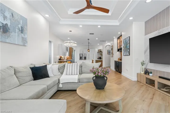 Living room featuring a raised ceiling, recessed lighting, light wood-style floors, ceiling fan, and a chandelier