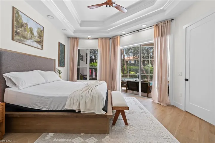 Bedroom with access to exterior, light wood finished floors, ornamental molding, a ceiling fan, and a raised ceiling