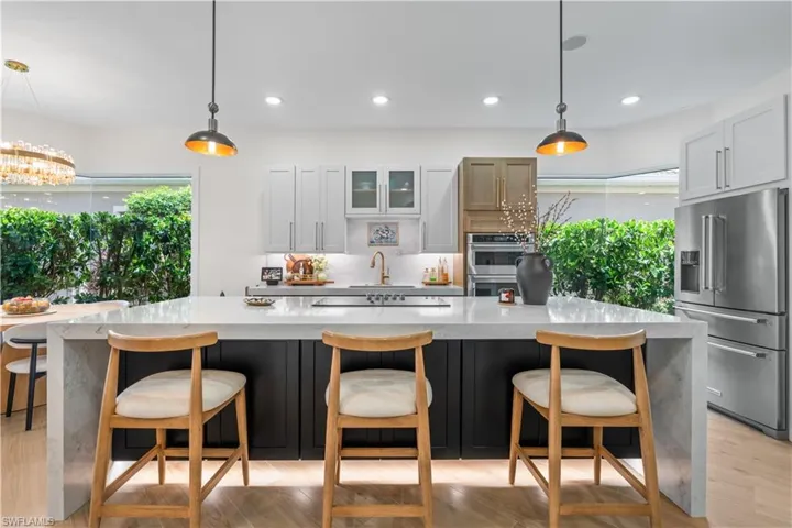 Kitchen featuring light wood-type flooring, appliances with stainless steel finishes, glass insert cabinets, recessed lighting, and decorative light fixtures