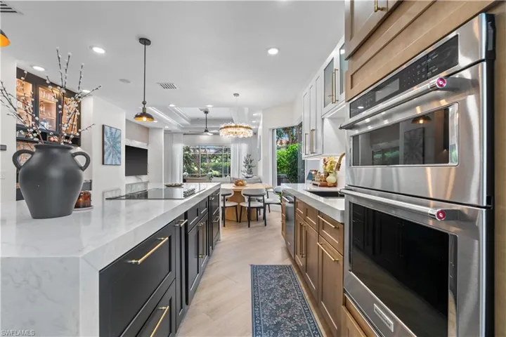 Kitchen featuring stainless steel appliances, light wood-style floors, a tray ceiling, light stone countertops, and hanging light fixtures
