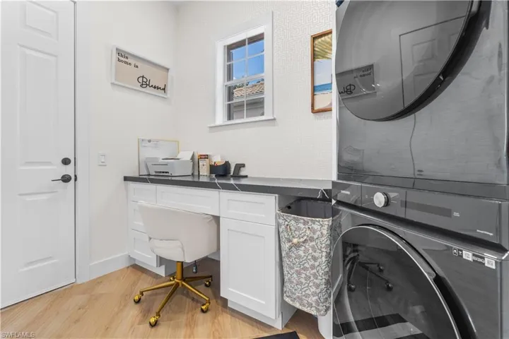 Laundry room with stacked washer and clothes dryer, a desk, cabinet space, and light wood-style flooring