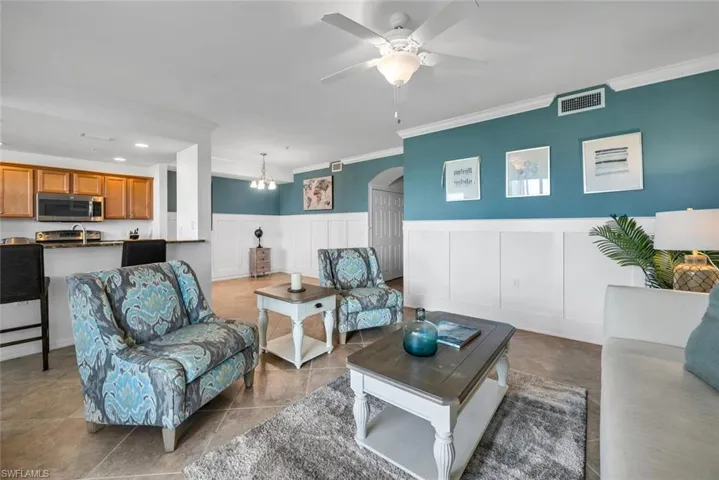 Living room with ceiling fan, light tile patterned floors, and crown molding