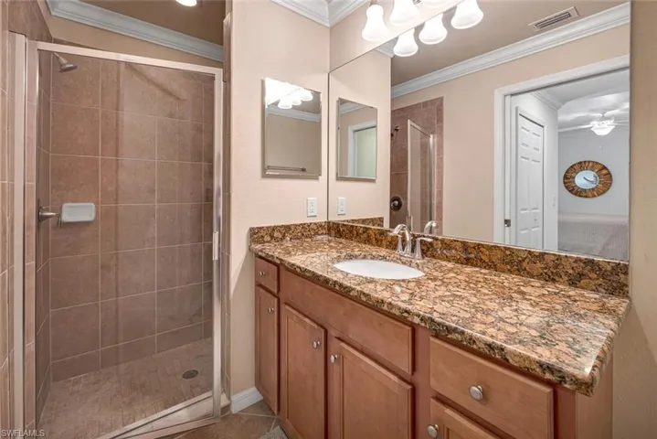 Bathroom with ornamental molding, ceiling fan, a shower with door, and vanity