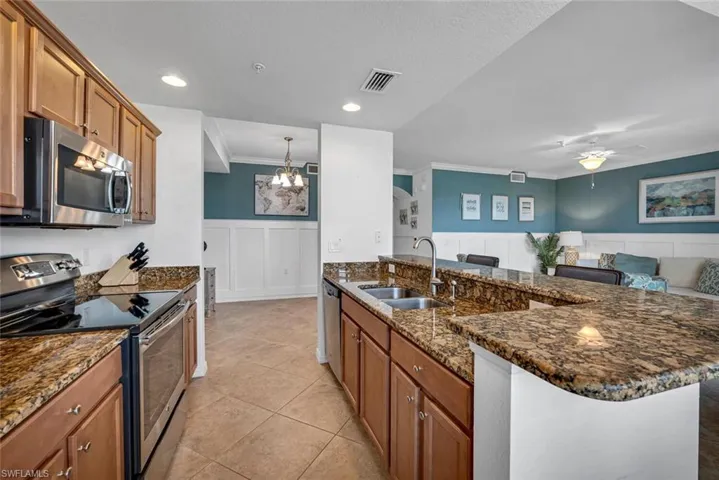 Kitchen with dark stone counters, sink, ceiling fan with notable chandelier, stainless steel appliances, and ornamental molding