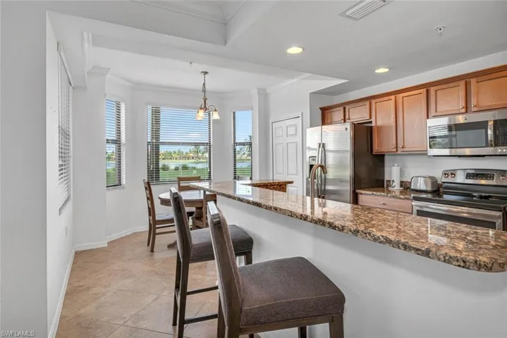 Kitchen featuring hanging light fixtures, a breakfast bar area, stainless steel appliances, crown molding, and dark stone counters