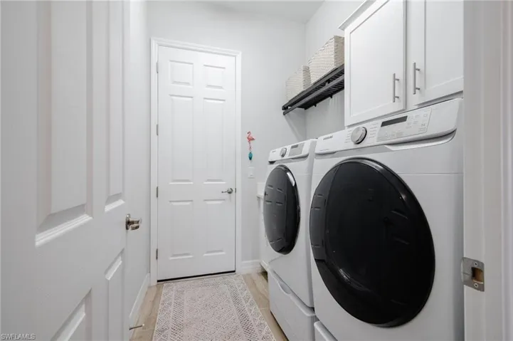 Clothes washing area with washing machine and clothes dryer, cabinets, and light hardwood / wood-style flooring