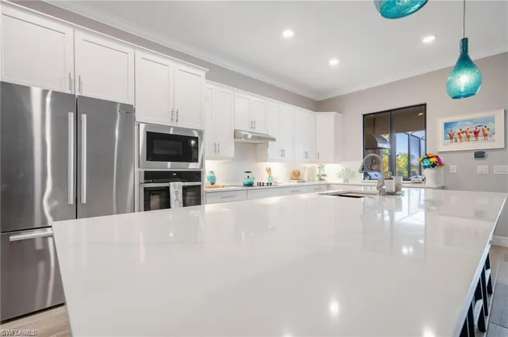 Kitchen featuring decorative light fixtures, sink, light stone countertops, white cabinets, and appliances with stainless steel finishes