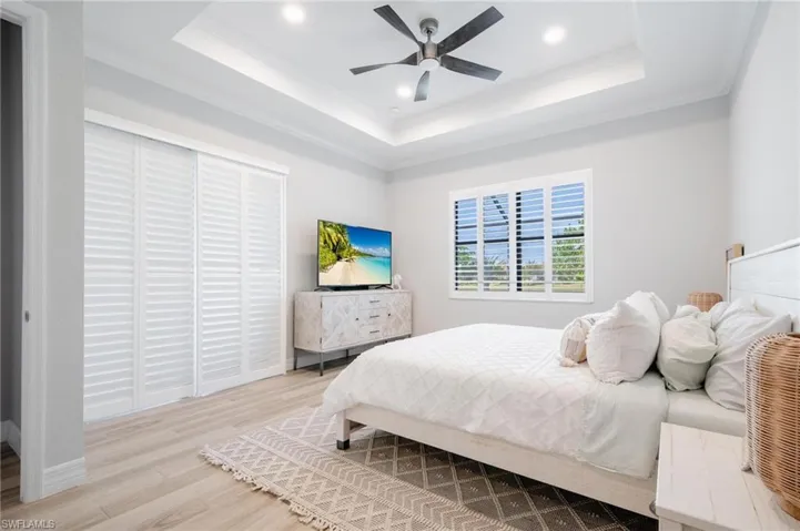 Bedroom with a raised ceiling, crown molding, light hardwood / wood-style flooring, and ceiling fan