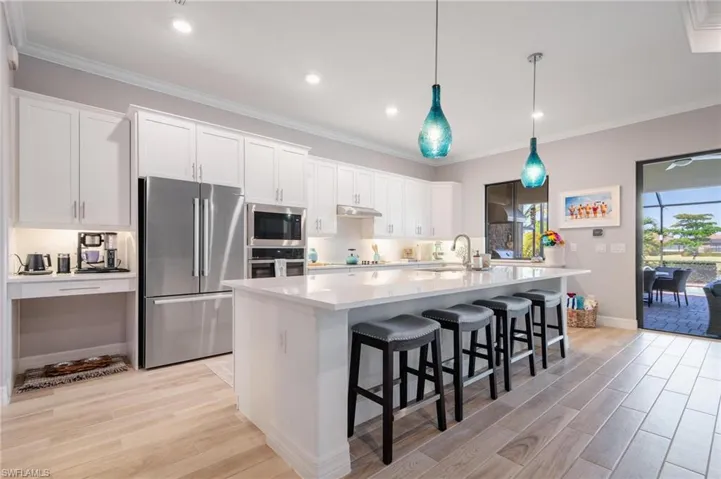 Kitchen with appliances with stainless steel finishes, light hardwood / wood-style floors, an island with sink, and white cabinets